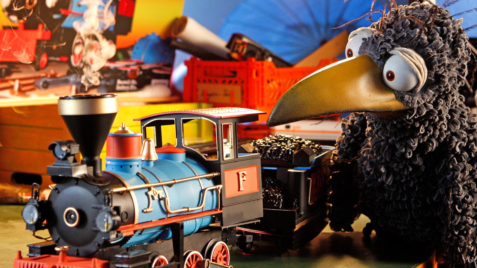 Rabe Rudi schaut eine Spielzeuglokomotive an