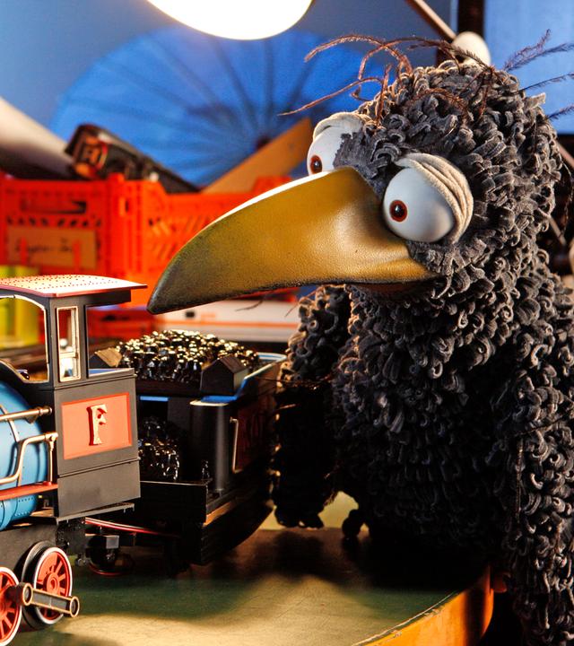 Rabe Rudi schaut eine Spielzeuglokomotive an