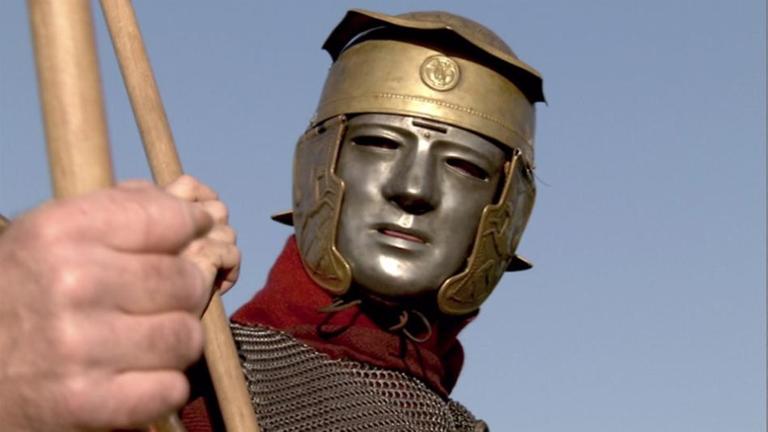 Spielszene: Römischer Soldat, der am Limes gedient hat, mit typischem Helm und eiserner Gesichtsmaske.