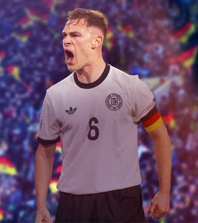 Nationalspieler und Kaptitän Josuah Kimmich in einem Fußballstadion mit Fans, von denen einige Deutschlandfahnen auf den Tribünen schwenken