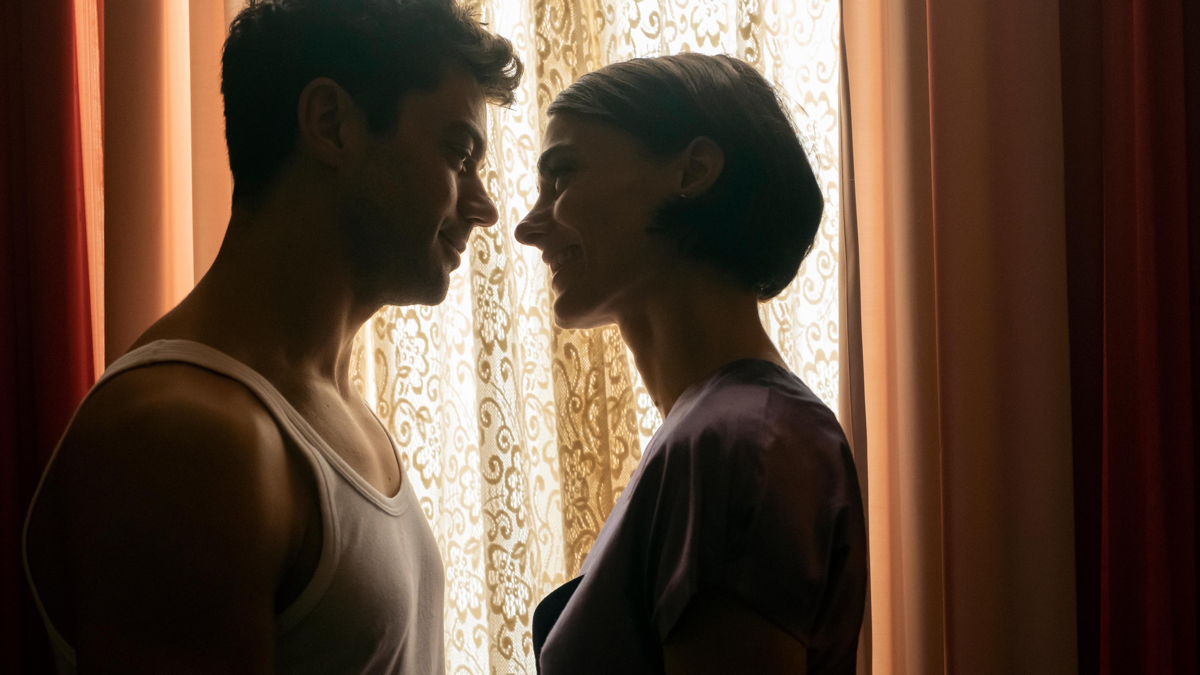"Spy City (1)": Fielding Scott (Dominic Cooper) und Severine Bloch (Romane Portail) stehen sich in einem Hotelzimmer an einem Fenster gegenüber und lächeln sich verliebt an.
