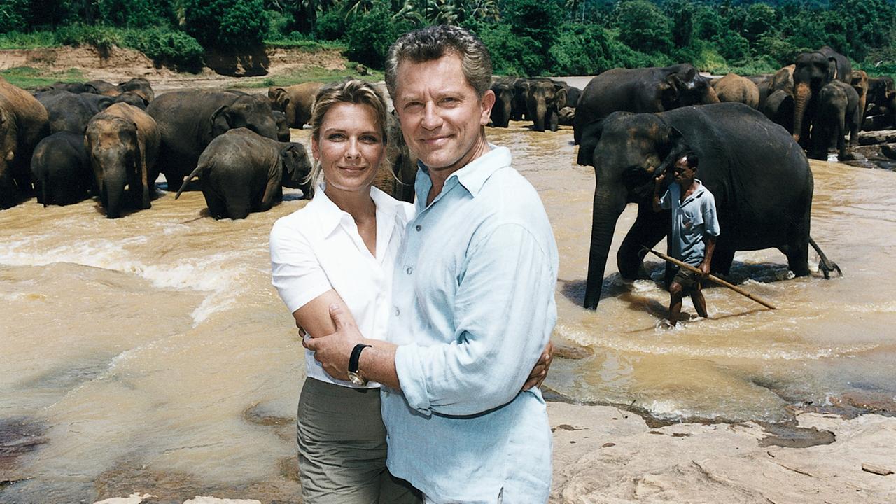 "Das Traumschiff - Sri Lanka": Ina (Janette Rauch) und Klaus (Miroslav Nemec) stehen Arm in Arm am Fluss und lächeln in die Kamera. Im Hintergrund steht eine Elefantenherde im Fluss, ein Elefant wird von einem Elefantenführer geleitet.