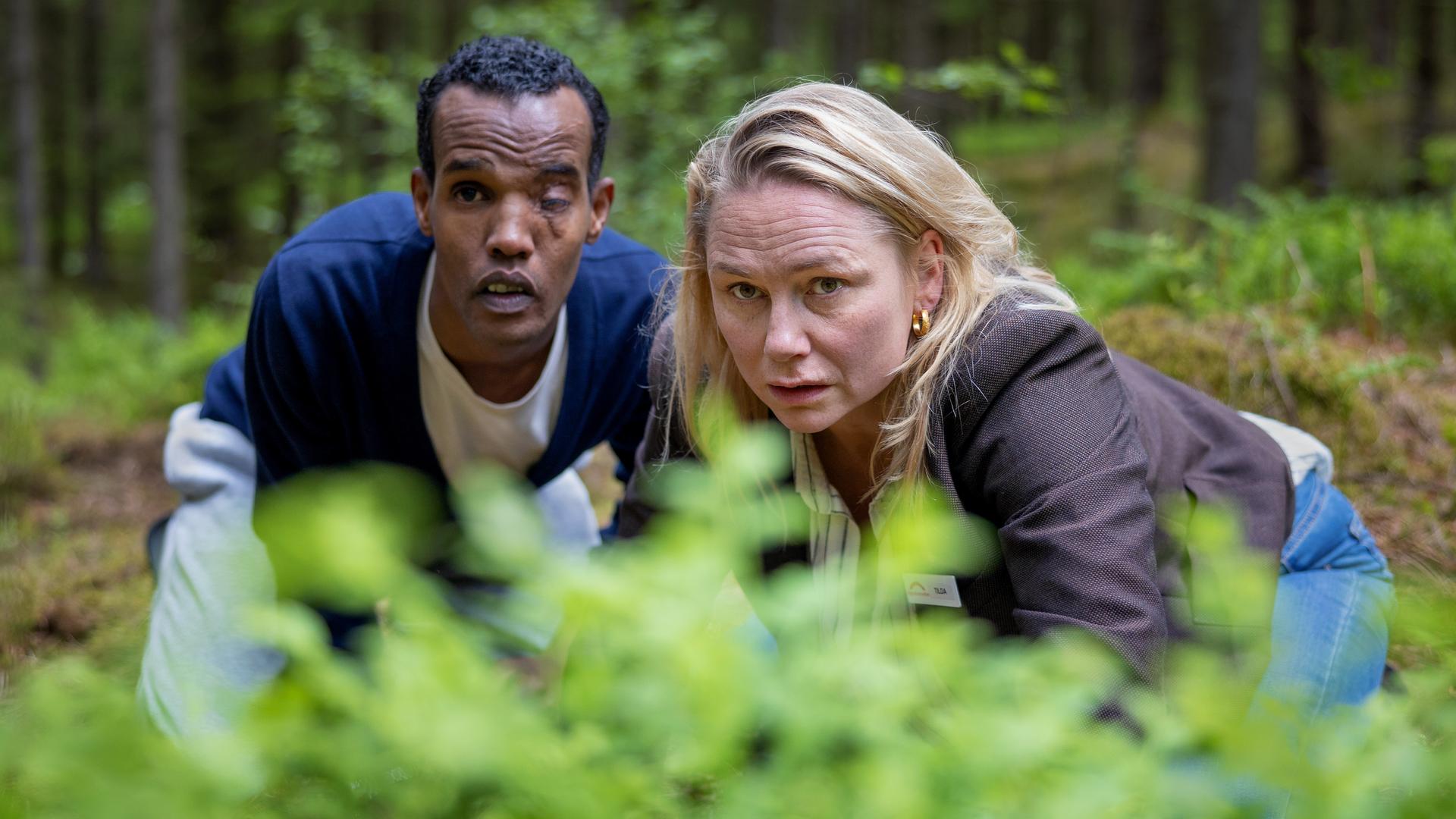 "Detective No. 24: Anna": Tilda (Malin Levanon) und Ibraahin (Nasir Farah Dhagole) knien im Wald hinter einem Gebüsch. Sie wollen nicht gesehen werden.