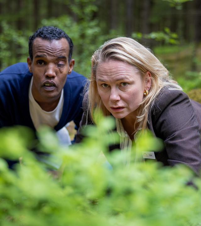 "Detective No. 24: Anna": Tilda (Malin Levanon) und Ibraahin (Nasir Farah Dhagole) knien im Wald hinter einem Gebüsch. Sie wollen nicht gesehen werden.