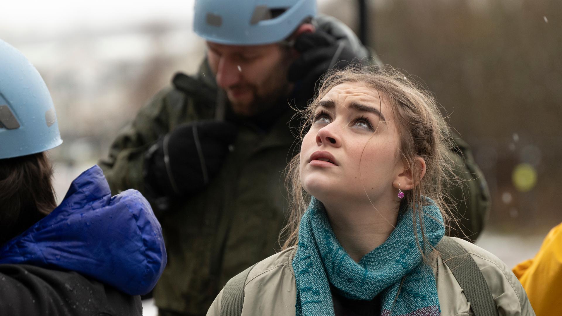Morgan Strandhed (Silvie Furneaux) blickt mit Sorgenfalten auf der Stirn skeptisch nach oben. Um den Hals trägt sie Sigis Schal. Um sie herum stehen Kletterer (Komparsen), die ihre Helmgurte schließen.