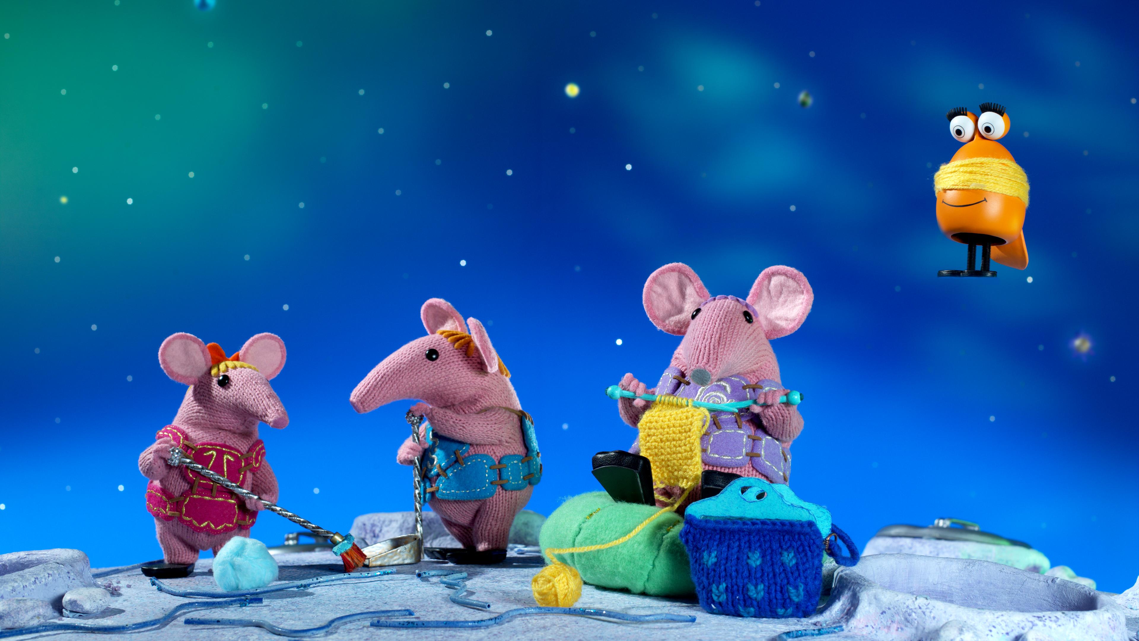 Auf dem Clanger Planeten machen die Geschwister Klitzeklein und Klein sauber. Klein hält eine Schaufel und Klitzeklein kehrt mit einem Besen. Daneben sitzt Oma Clanger auf einem Kissen und strickt. Ein Fröschlie kommt angeflogen und hat Wolle um sich gewickelt.
