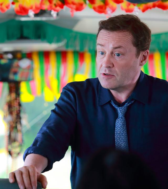 "Death in Paradise - Der Tote im Bus": DI Jack Mooney (Ardal O'Hanlon) und Butterfly Brown (Chizzy Akudolu) stehen in einem Bus nebeneinander und haben einen ernsten Blick.
