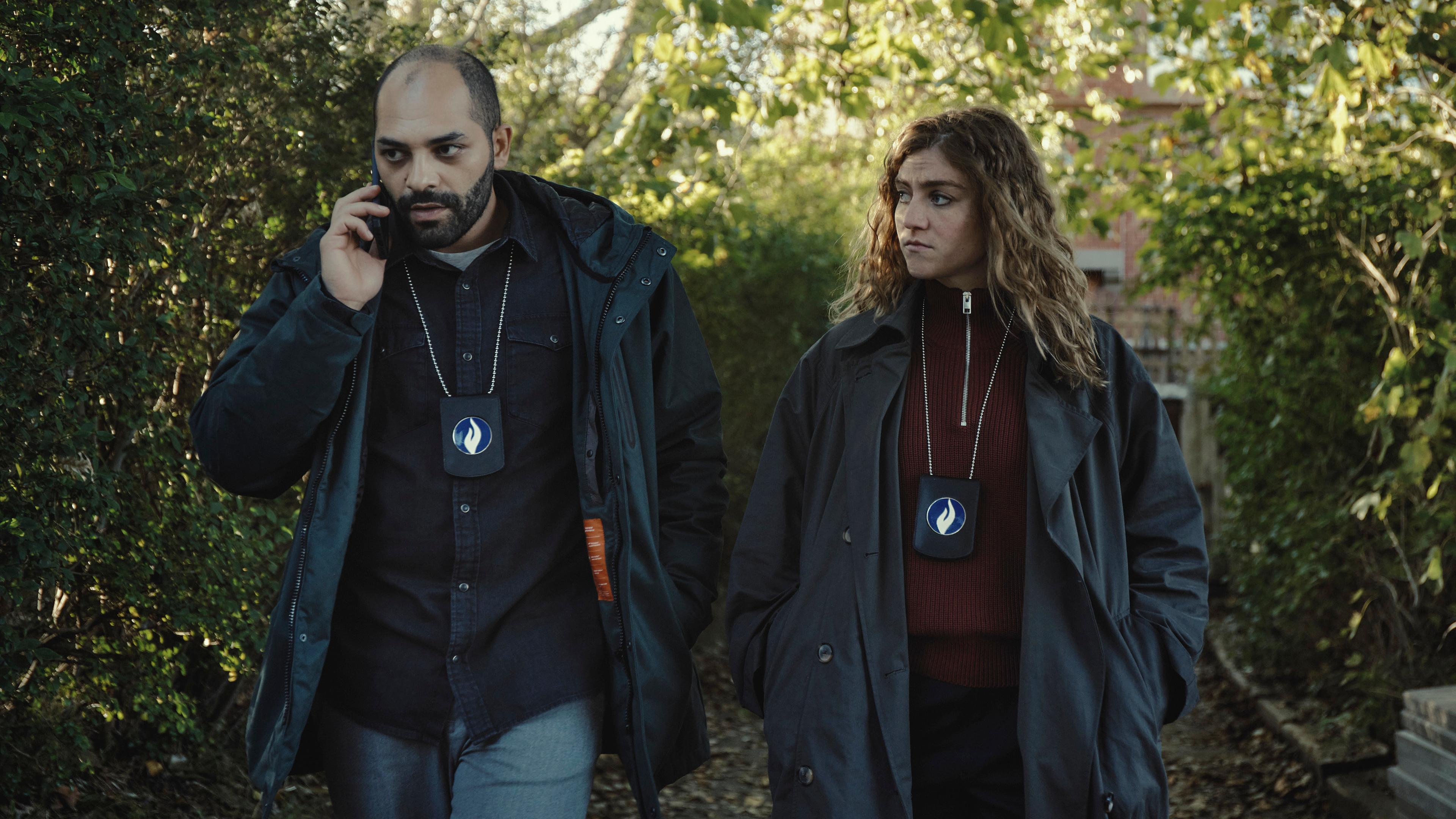 "Juliet - Die Tote im Kanal": Jamal (Nabil Mallat) und Juliet (Charlotte De Bruyne) gehen in einem Garten nebeneinander. Er telefoniert. Sie schaut in Jamals Richtung.