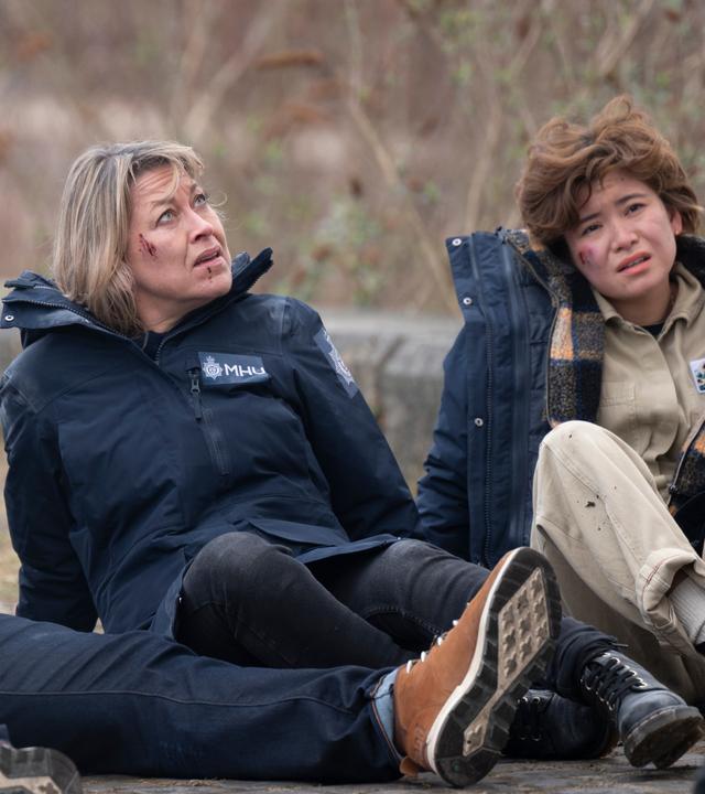 "Annika - Mord an Schottlands Küste - Familie": Tyrone Clarke (Ukweli Roach), Annika Strandhed (Nicola Walker) und Blair Ferguson (Katie Leung) sitzen im Freien auf dem Boden, sie haben Schrammen im Gesicht und blicken erschöpft.