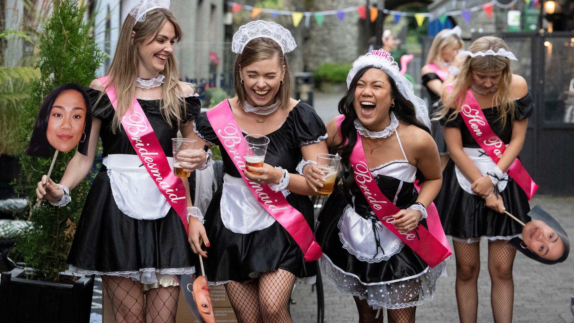 Sinead (Sorcha Fahy), Niamh (Juliette Crosbie) und Charlotte (Rhea Rose Rodillas) gehen nebeneinander durch eine Straße, in der mehrere Bars ansässig sind. Alle drei lachen. Holly (Ali Hardiman) bleibt etwas zurück und schaut nach unten. Noch weiter im Hintergrund steht Aisling (Sophie Vavasseur). Alle Frauen tragen Hausmädchen-Kostüme und pinkfarbene Schärpen.