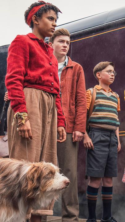 "Fünf Freunde - Das Abenteuer im Nachtzug": Timmy (Kip), George (Diaana Babnicova), Julian (Elliott Rose), Dick (Kit Rakusen) und Anne (Flora Jacoby Richardson) stehen nebeneinander auf einem Bahnsteig. Hinter ihnen steht ein Zug, in den gerade Menschen (Komparsen) einsteigen.