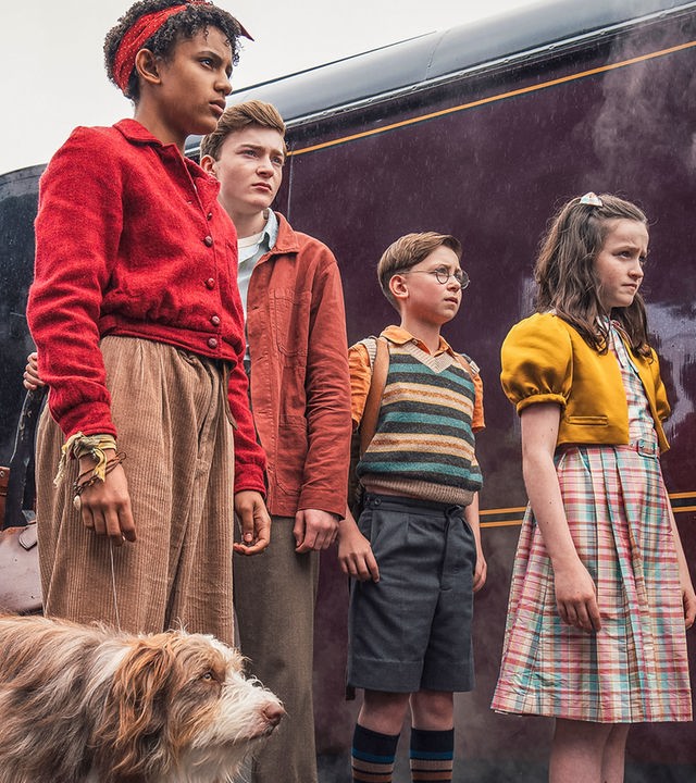 "Fünf Freunde - Das Abenteuer im Nachtzug": Timmy (Kip), George (Diaana Babnicova), Julian (Elliott Rose), Dick (Kit Rakusen) und Anne (Flora Jacoby Richardson) stehen nebeneinander auf einem Bahnsteig. Hinter ihnen steht ein Zug, in den gerade Menschen (Komparsen) einsteigen.