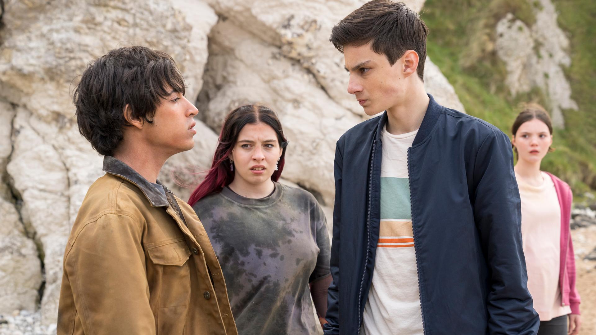 Am Strand vor hellem Felsen stehen sich Louis, gespielt von Oliver Cunliffe, und Jay, gespielt von Noah Manzoor, gegenüber. Louis ist voller Wut mit angespanntem Gesicht und geballten Fäusten. Jay schaut ihn herausfordernd an. Die beiden werden von Kaz, gespielt von Maiya Silveston, und Isabel, gespielt vo Alis Waters, beobachtet. Kaz schaut mit einem verächtlichen Blick zu Jay.