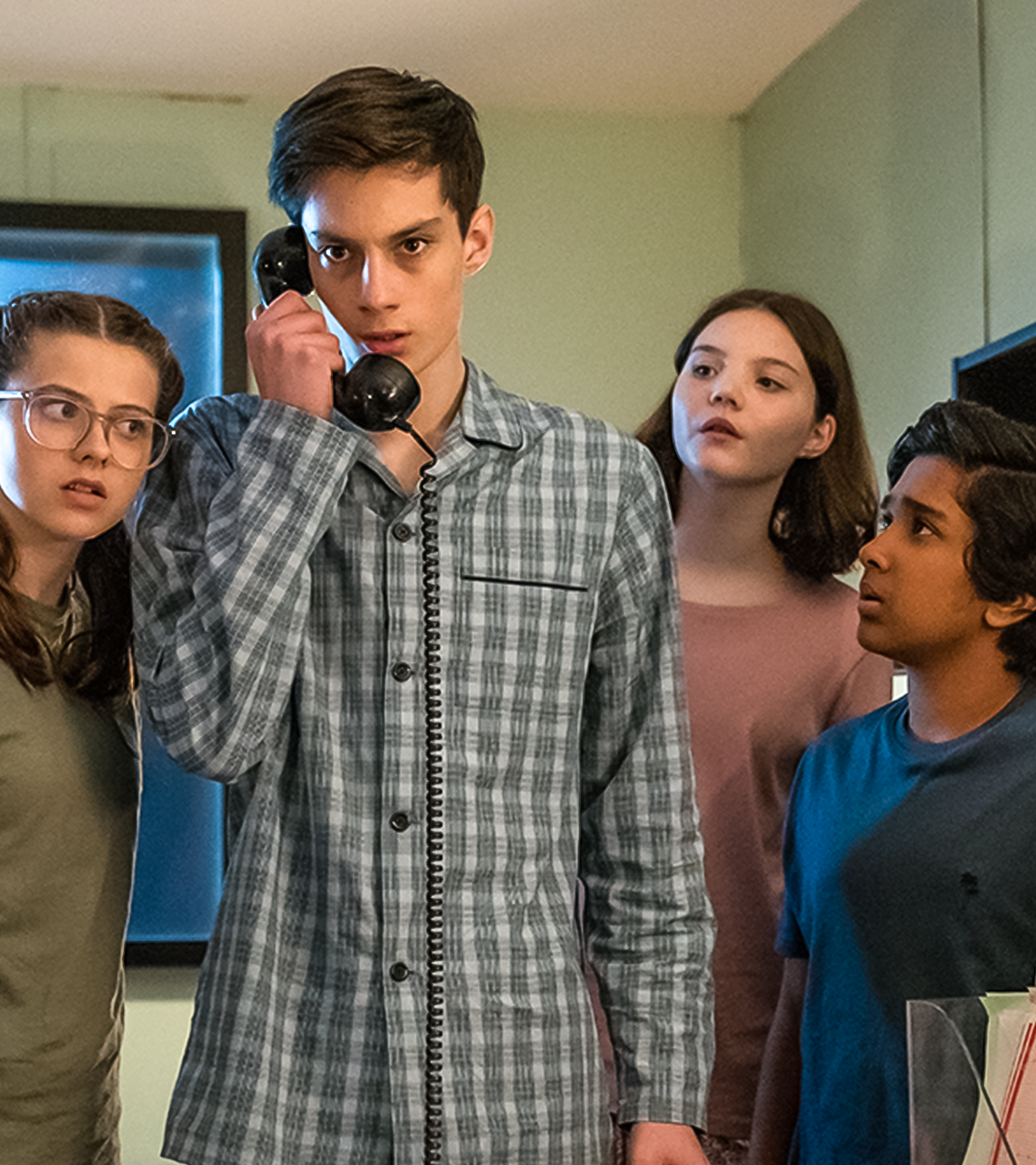 In einem Büroraum bei Nacht stehen Monika, gespielt von Lucy Chambers, Isabel, gespielt von Alis Waters, und Glen, dargestellt von Krish Misra, um Louis, Darsteller Oliver Cunliffe, herum. Louis hält einen alten schwarzen Telefonhörer in der Hand. Die drei schauen neugierig und aufmerksam zu Louis, während dieser ernst nach vorne schaut. Alle tragen Schlafanzüge.