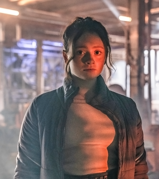 In einer großen Halle, in der eine riesige Plastikplane wie eine Wand gespannt ist: Bea schaut konzentriert nach vorne und hat eine Stoppuhr in ihrer linken Hand.