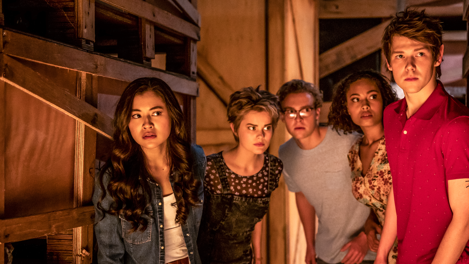 Kyra, Imogen, Peter, Ruksy und Darra stehen dicht nebeneinander in einem dunklen Raum zwischen Holzregalen. Sie schauen vorsichtig und aufmerksam in eine Richtung.