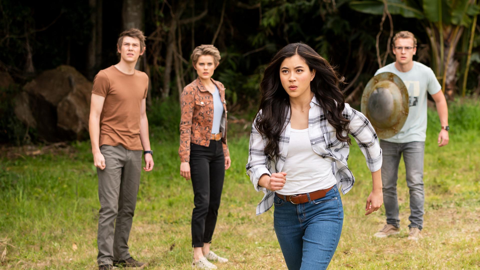 Darra, Imogen, Peter, Ruksy und Lily stehen hinter Kyra auf einer Wiese, die von dichtem Wald umgeben ist. Kyra beginnt, auf ein vor ihr liegendes Ziel loszurennen. Ruksy und Lily strecken ihre Zauberstäbe nach vorne, Peter hält ein Metallschild in der rechten Hand vor dem Körper. Alle sind angespannt und schauen ernst nach vorne.