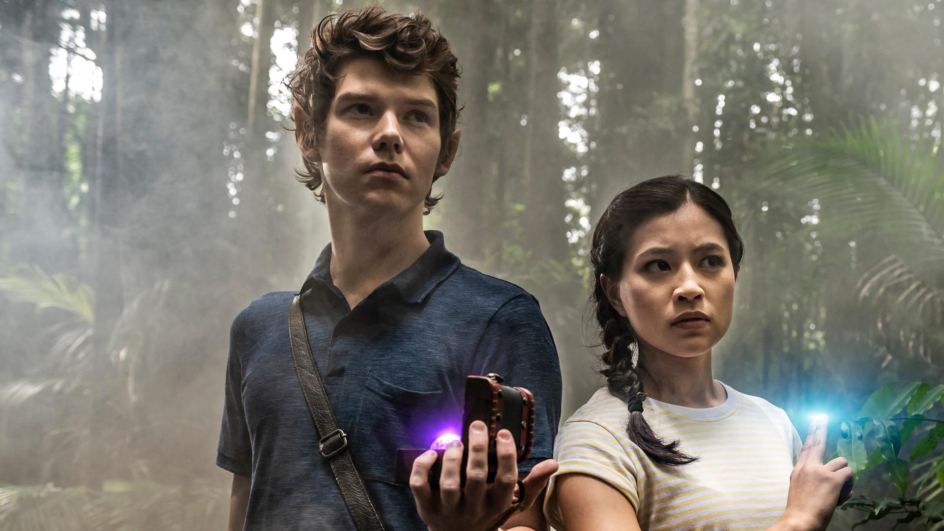 Kyra und Darren stehen nebeneinander im Wald. Zwei Finger an der rechten, leicht erhobenen Hand von Kyra leuchten blau. Darra hat seine Tasche über Kreuz umhängen. In seiner linken Hand hält er eine kleine, geöffnete Holzbox, in der eine Kugel leuchtet.