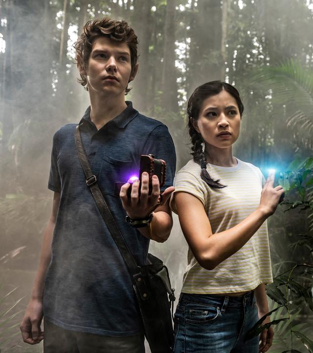 Kyra und Darren stehen nebeneinander im Wald. Zwei Finger an der rechten, leicht erhobenen Hand von Kyra leuchten blau. Darra hat seine Tasche über Kreuz umhängen. In seiner linken Hand hält er eine kleine, geöffnete Holzbox, in der eine Kugel leuchtet.