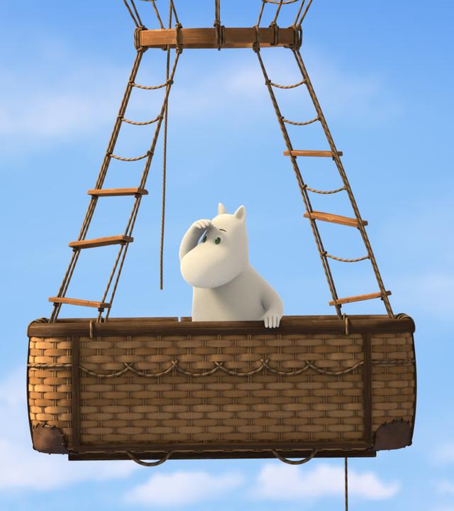 Hoch oben in den Lüften: Muminmama (Mitte) steht im Korb eines fliegenden Heißluftballons. Die Hand hält sie über die Augen und schaut ins Weite.