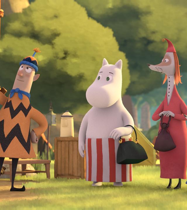 Auf einem Zeltplatz im Wald stehen neben einem Zelt Herr Frisch (links) mit Mütze und Pullover sowie Pfadfinderschal. Muminmama (2.v.l.) und Frau Fillifjonk (3.v.l.) sowie die drei Nichten von Frau Fillifjonk (rechts) lauschen gebannt was der Campingmeister Frisch erklärt.