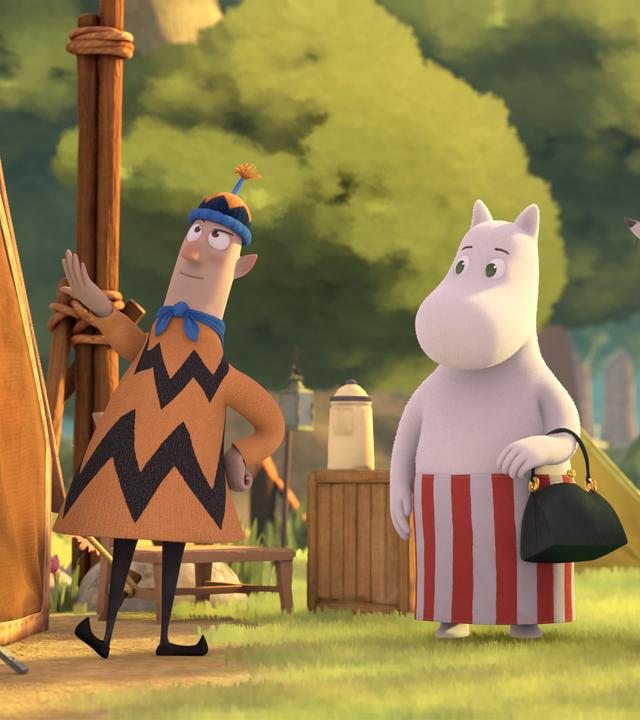 Auf einem Zeltplatz im Wald stehen neben einem Zelt Herr Frisch mit Mütze und Pullover sowie Pfadfinderschal. Muminmama und Frau Fillifjonk sowie die drei Nichten von Frau Fillifjonk lauschen gebannt was der Campingmeister Frisch erklärt.