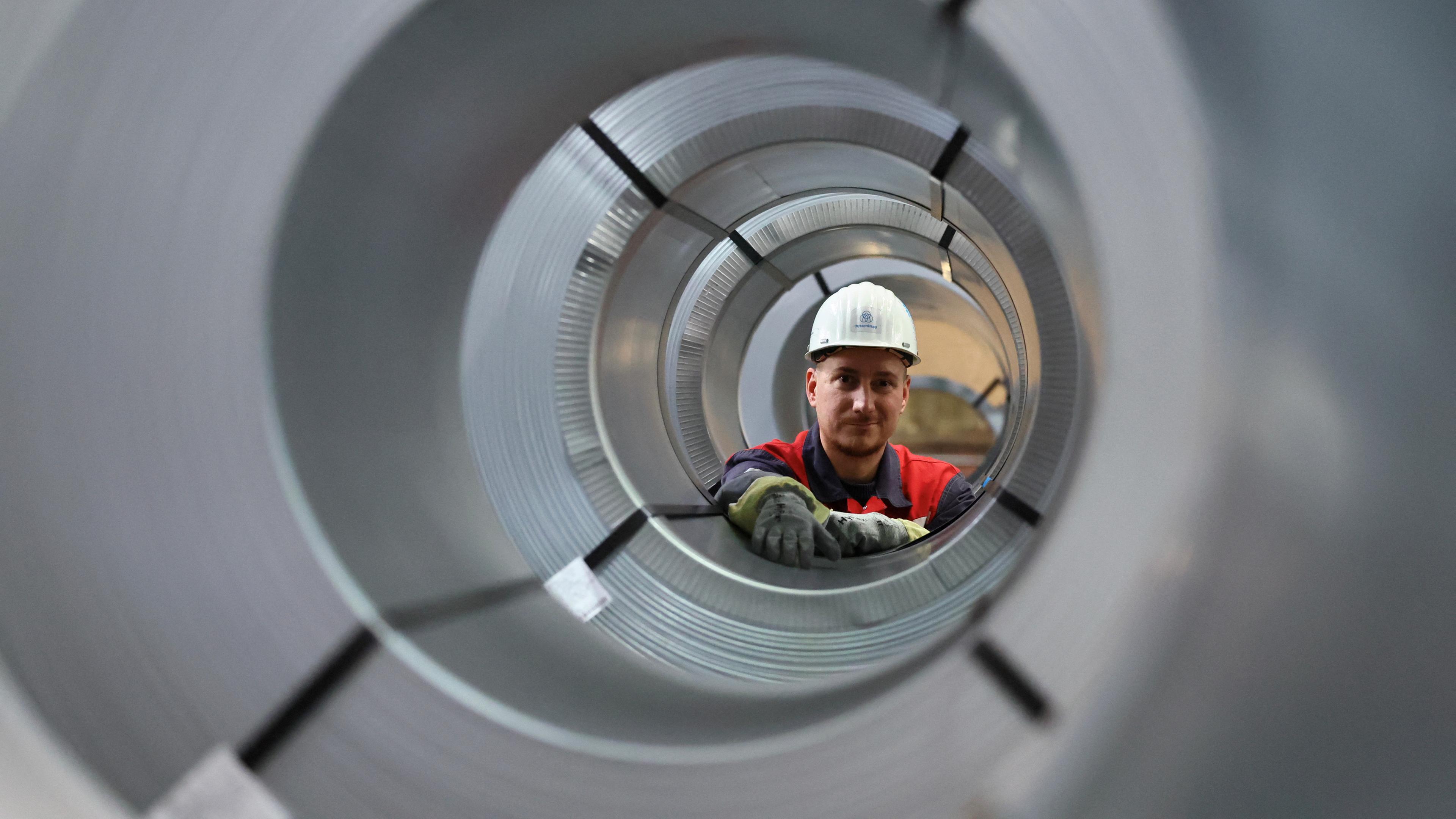 Archiv: Ein Stahlarbeiter posiert für ein Foto, während er durch Stahlspulen in der Lager- und Vertriebsanlage des deutschen Stahlherstellers ThyssenKrupp in Duisburg schaut, 16. November 2023.