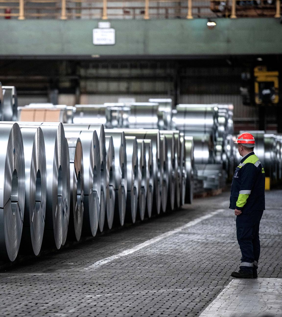 Ein Arbeiter steht vor Stahlspulen der Thyssenkrupp Steel Europe AG