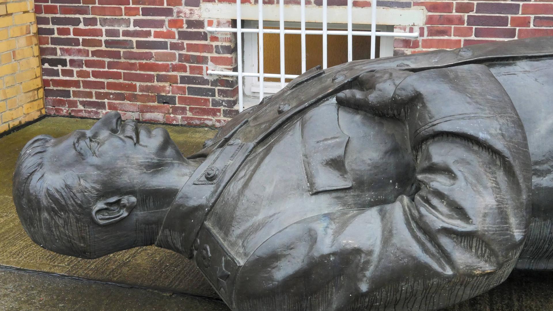 Eine Männrestatue liegt auf dem Rücken in einem Hof.