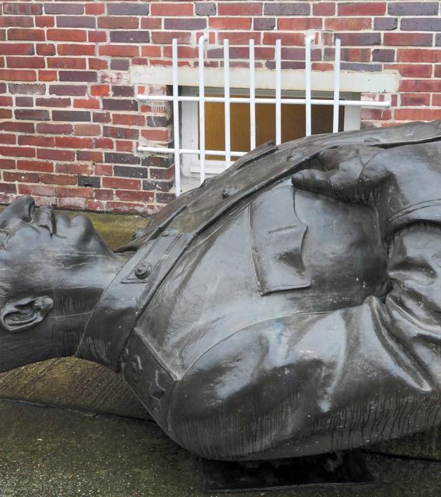 Eine Männrestatue liegt auf dem Rücken in einem Hof.