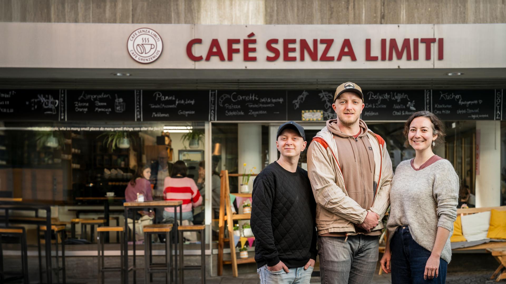 Fabian Karl, Steven Henze und Franziska Kling stehen als Gruppe vor dem Café Senza Limiti. Am Haus ist der Name des Cafés angebracht.