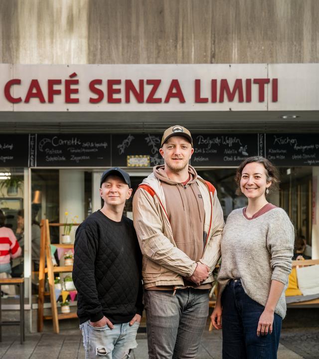 Fabian Karl, Steven Henze und Franziska Kling stehen als Gruppe vor dem Café Senza Limiti. Am Haus ist der Name des Cafés angebracht.