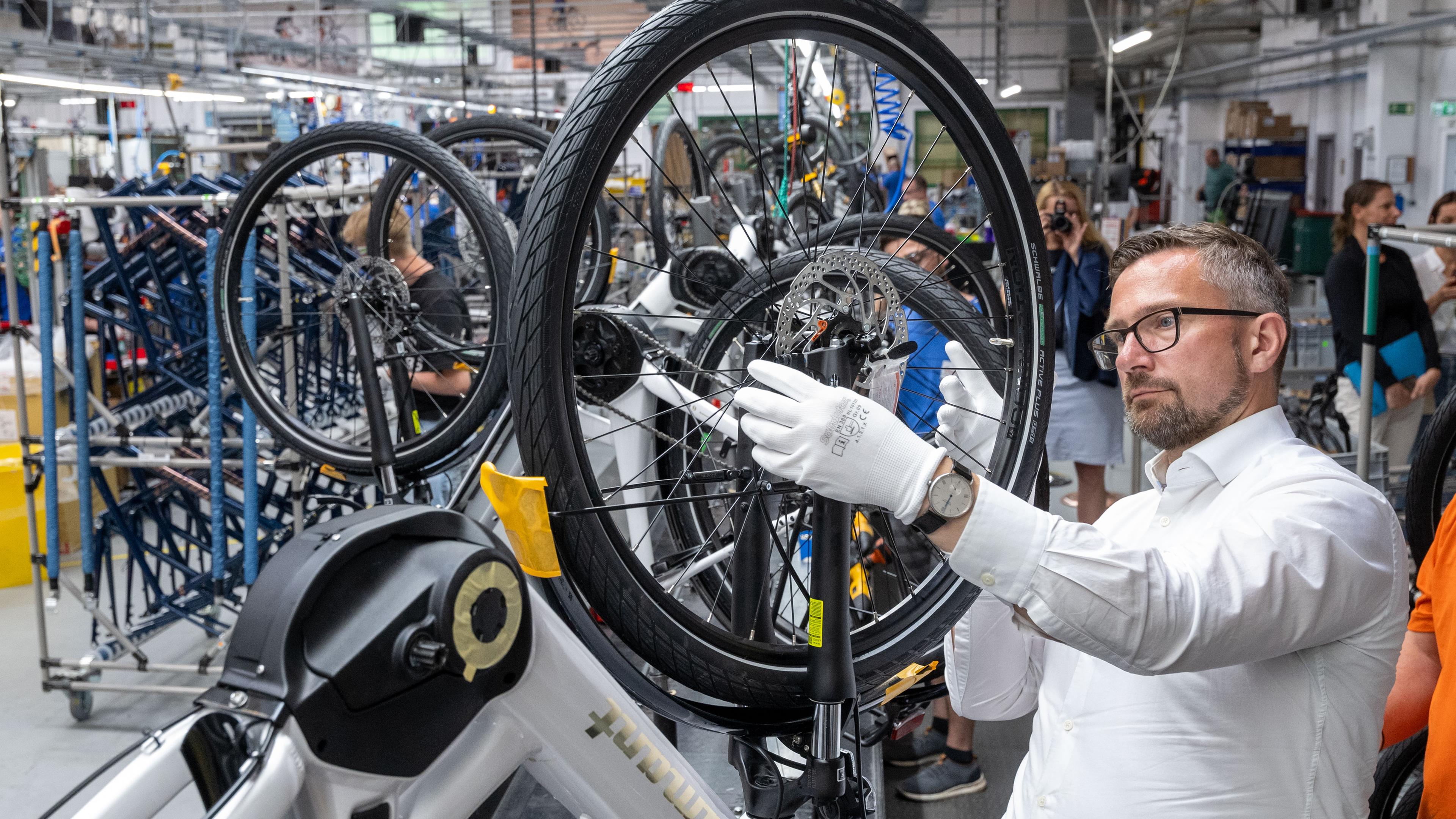 Sachsen, Hartmannsdorf: Martin Dulig (SPD), Wirtschaftsminister in Sachsen, montiert in der Produktion des Fahrradherstellers Diamant in Hartmannsdorf das Vorderrad an einem E-Bike.