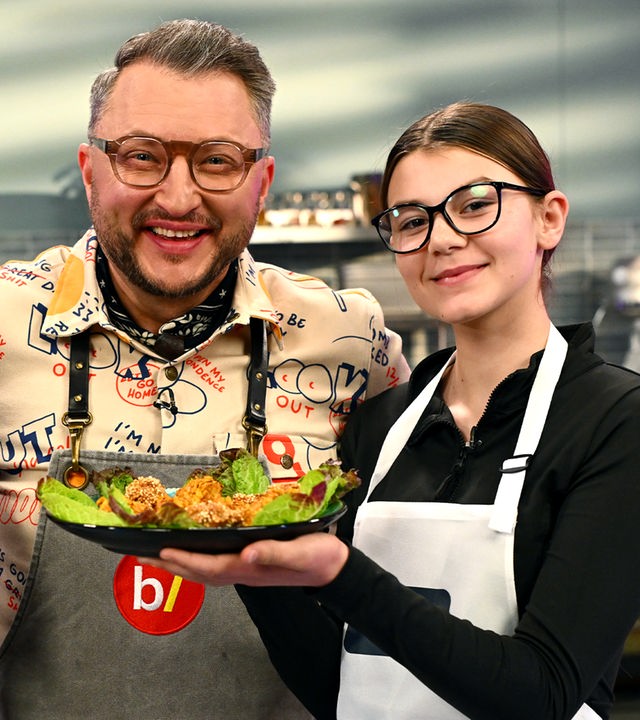 "besseresser Kids": Bibi (l.) und Lucy (r.) zeigen lächelnd ein Tablett voller selbstgemachter Chicken Nuggets mit verschiedenen knusprigen Panaden. Sebastian Lege (m.) blickt zwischen den beiden hervor. Die drei tragen Schürzen und stehen vor der Küchenzeile des Besseresser-Küchenstudios.