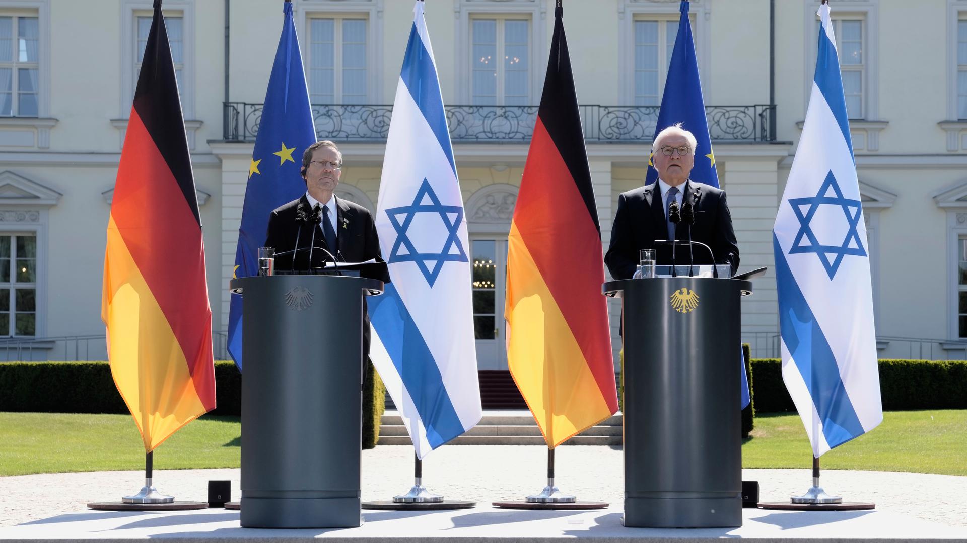 Zwei Männer stehen vor deutschen und israelischen Flaggen an Stehpulten.