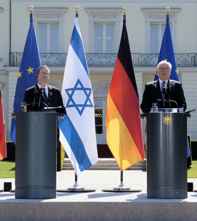 Zwei Männer stehen vor deutschen und israelischen Flaggen an Stehpulten.