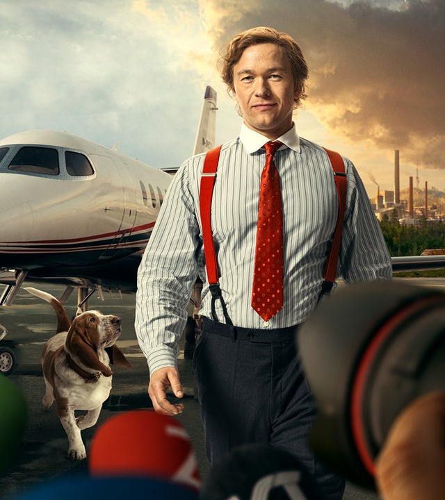 Stenbeck steht, in einem gestreiften Hemd mit roter Krawatte und roten Hosenträgern, auf einem Flugfeld. Sein Hund, ein braun-weißer Basset, schaut von links unten hoch zu ihm. Direkt hinter ihm steht ein moderner Privat-Jet. Im Hintergrund sieht man eine geteilte Landschaft, links die New Yorker Skyline, rechts eine ländliche Landschaft mit einer rauchenden Fabrik darauf. Der Himmel über New York ist weitgehend klar und blau, über der Fabrik ziehen dunkle, rötlich gefärbte Wolken. Im Vordergrund sind Kameras und Mikrofone aufgebaut.