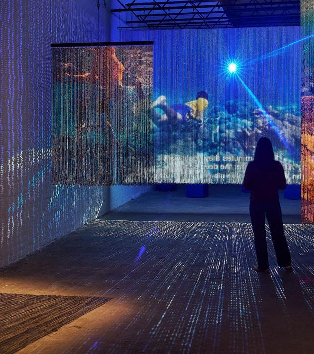 Die dunklen Umrisse zweier Personen, die vor an die Wände projizierten Bildern stehen.