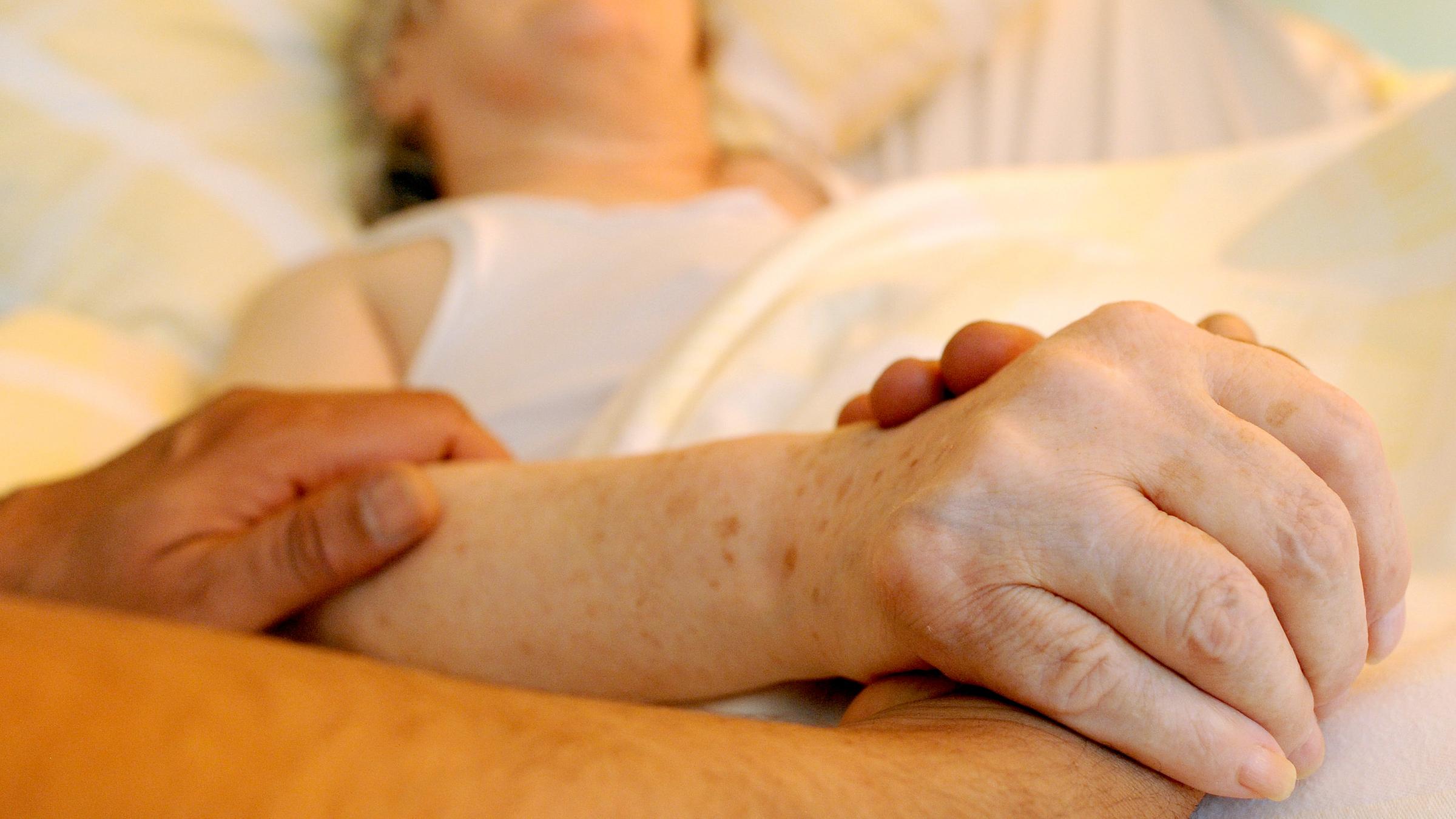 Ein Pfleger hält die Hand einer alten Frau 