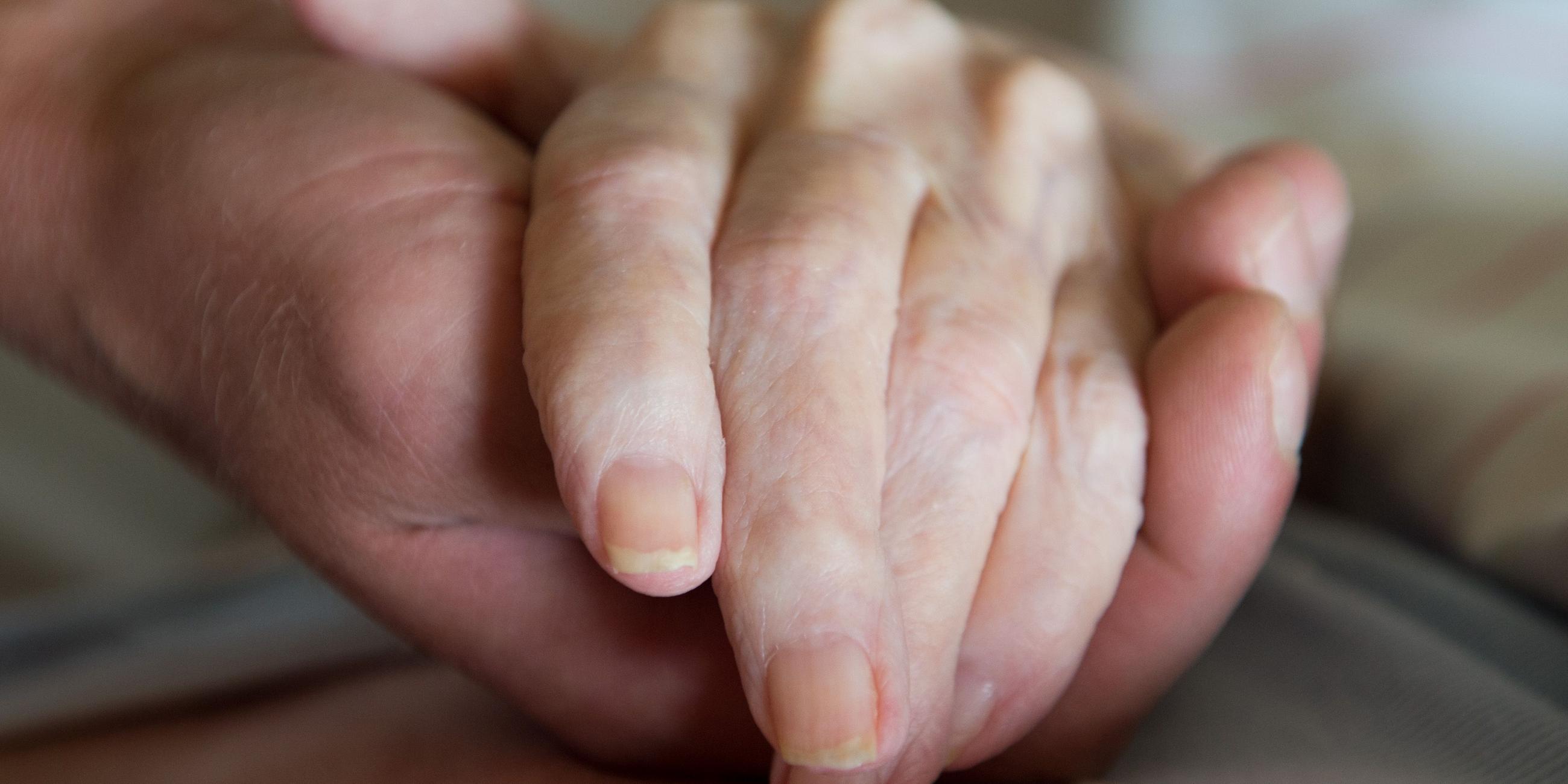 Ein Altenpfleger hält in einem Pflegeheim die Hand einer Frau. 