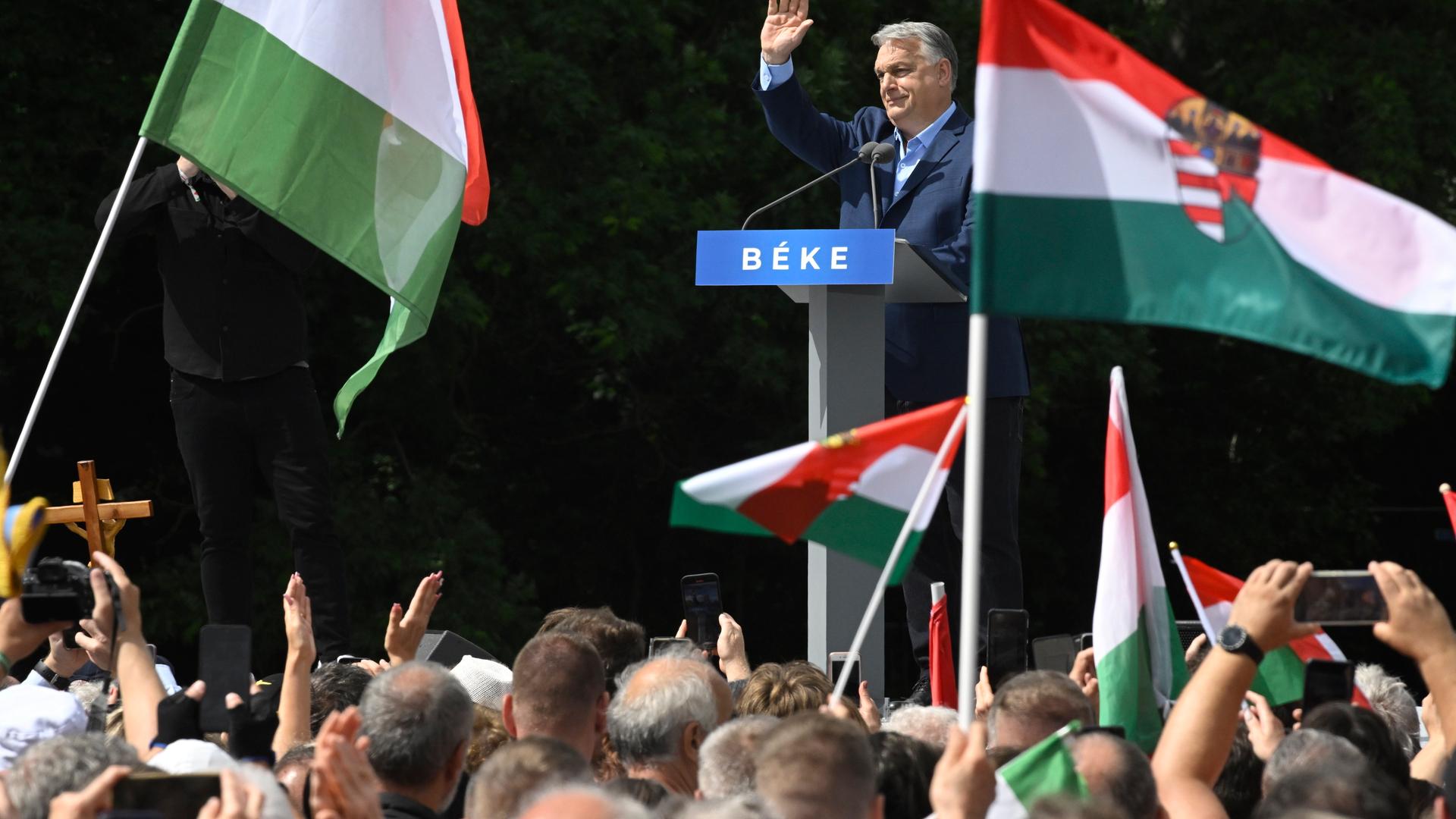 Der ungarische Premierminister Viktor Orbán spricht während eines Antikriegs-Friedensmarsches in Budapest. Er winkt vielen, den vor ihm versammelten Menschen, zu, die teilweise die ungarishe Flagge schwenken.