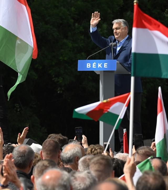 Der ungarische Premierminister Viktor Orbán spricht während eines Antikriegs-Friedensmarsches in Budapest. Er winkt vielen, den vor ihm versammelten Menschen, zu, die teilweise die ungarishe Flagge schwenken.