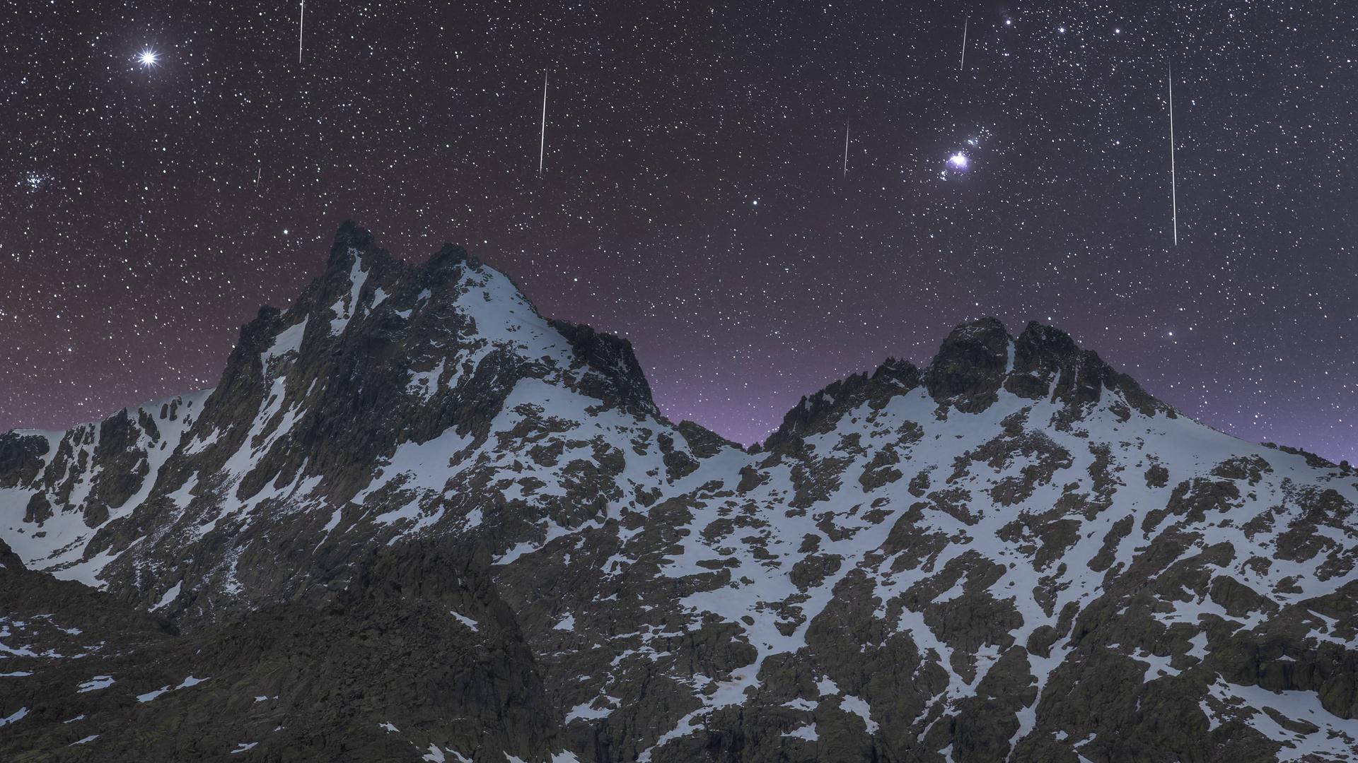 Sternschnuppen am  Nachthimmel über einem Gebirge.