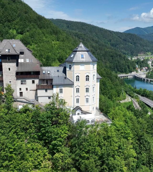 Luftaufnahme von Schloss Klaus im Steyrtal, Oberösterreich, gelegen am bewaldeten Hang über der Steyr mit Blick auf den Fluss und umliegende Berge.