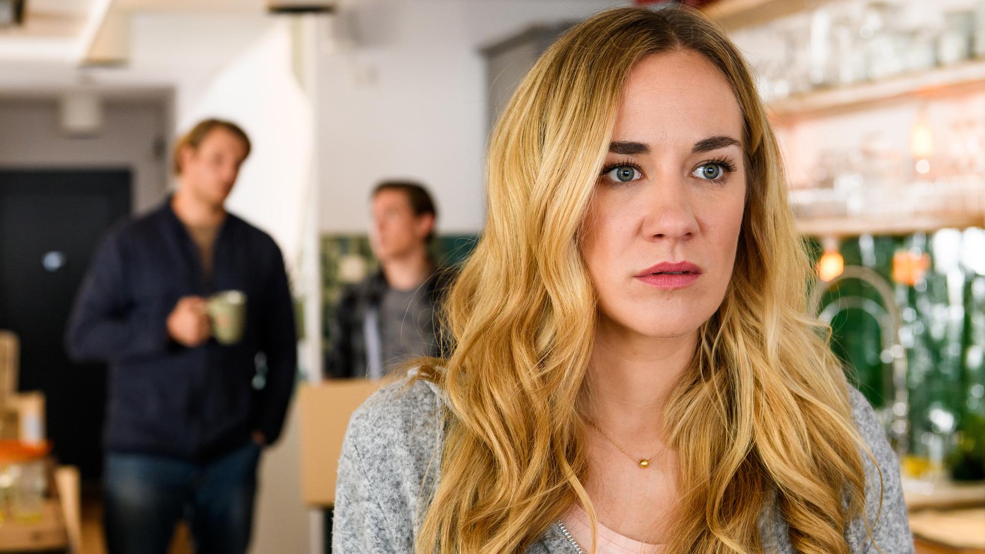 "Bettys Diagnose - Stillgestanden": Betty Weiss (Annina Hellenthal) schaut emotional berührt ins Leere, während Oliver Weiss (Alexander Koll) und Yannick Weiss (Alvar Goetze) im Hintergrund miteinander sprechen.