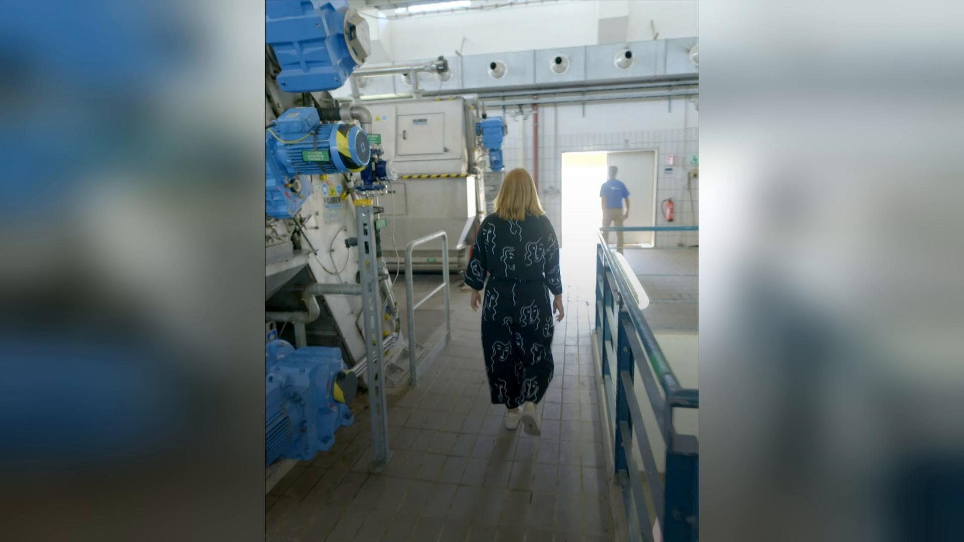 Zwei Personen sind von hinten zu sehen, wie sie auf eine Kläranlage zulaufen. 