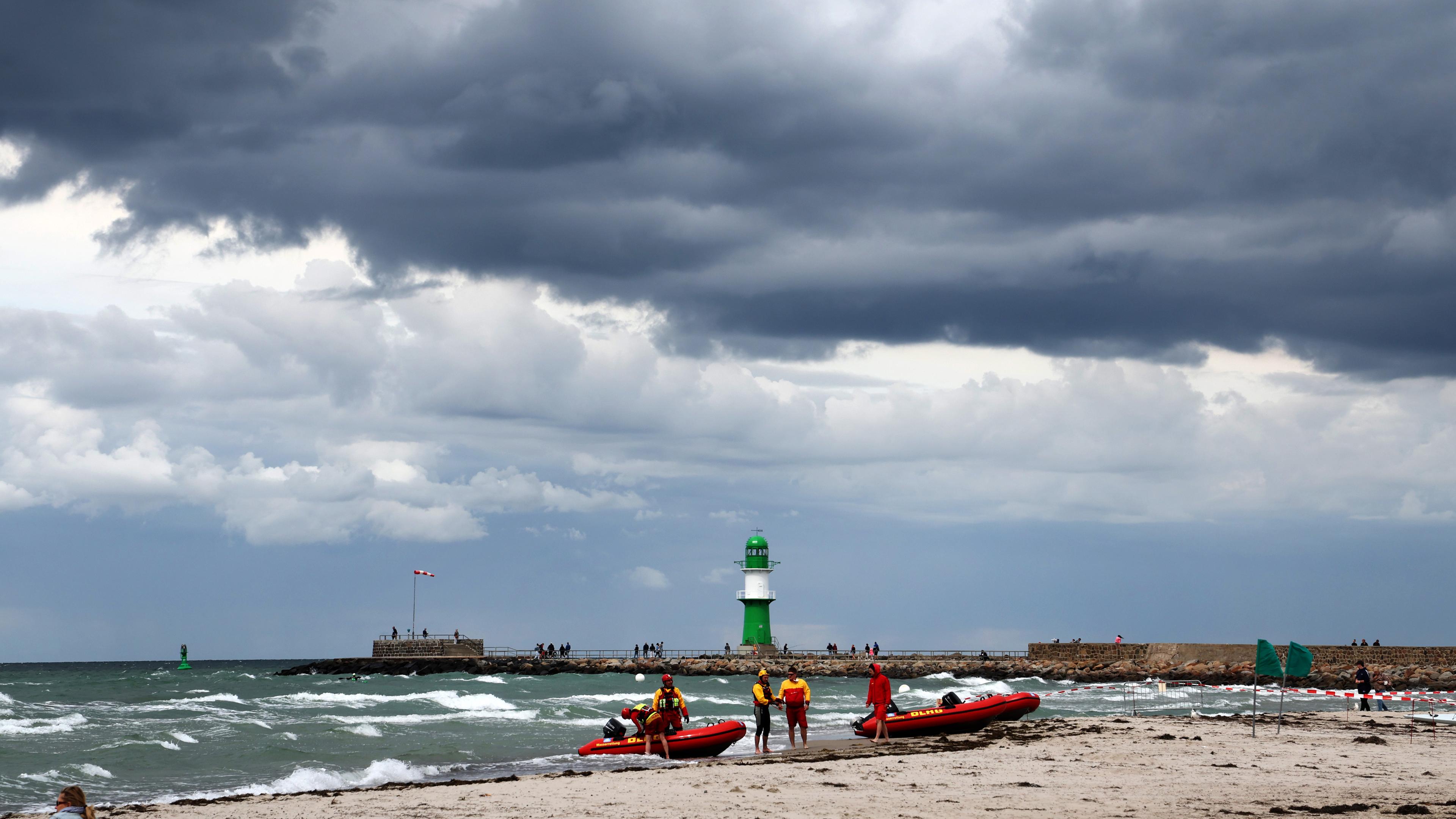 Der Strand von Warnemünde: Im Vordergrund sind zwei rote Boote. Im Hintergrund kann man einen grünen Leuchtturm erkennen.