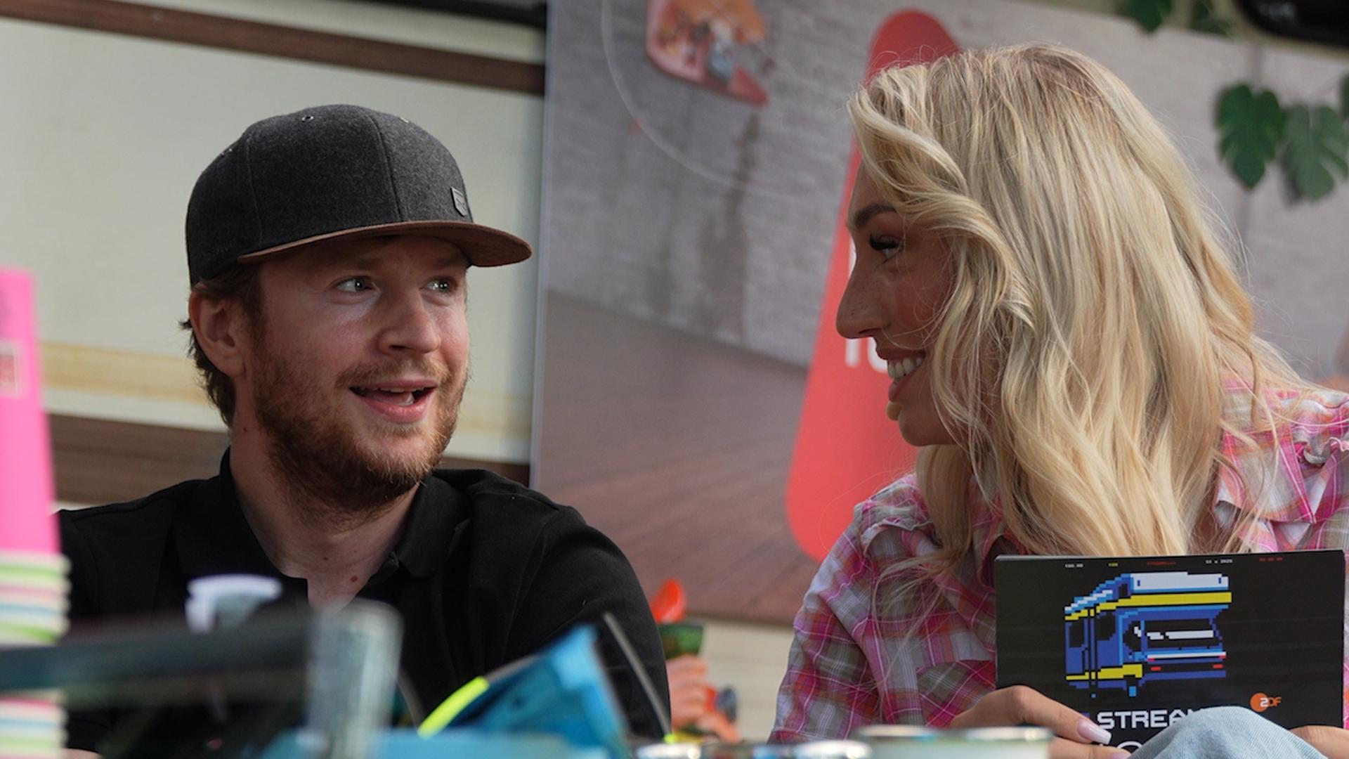 "Streamergarten -Folge 1: Die absoluten Highlights": Host Nova (r.) und ein Gast sitzen vor dem Streamergarten-Campermobil und unterhalten sich.