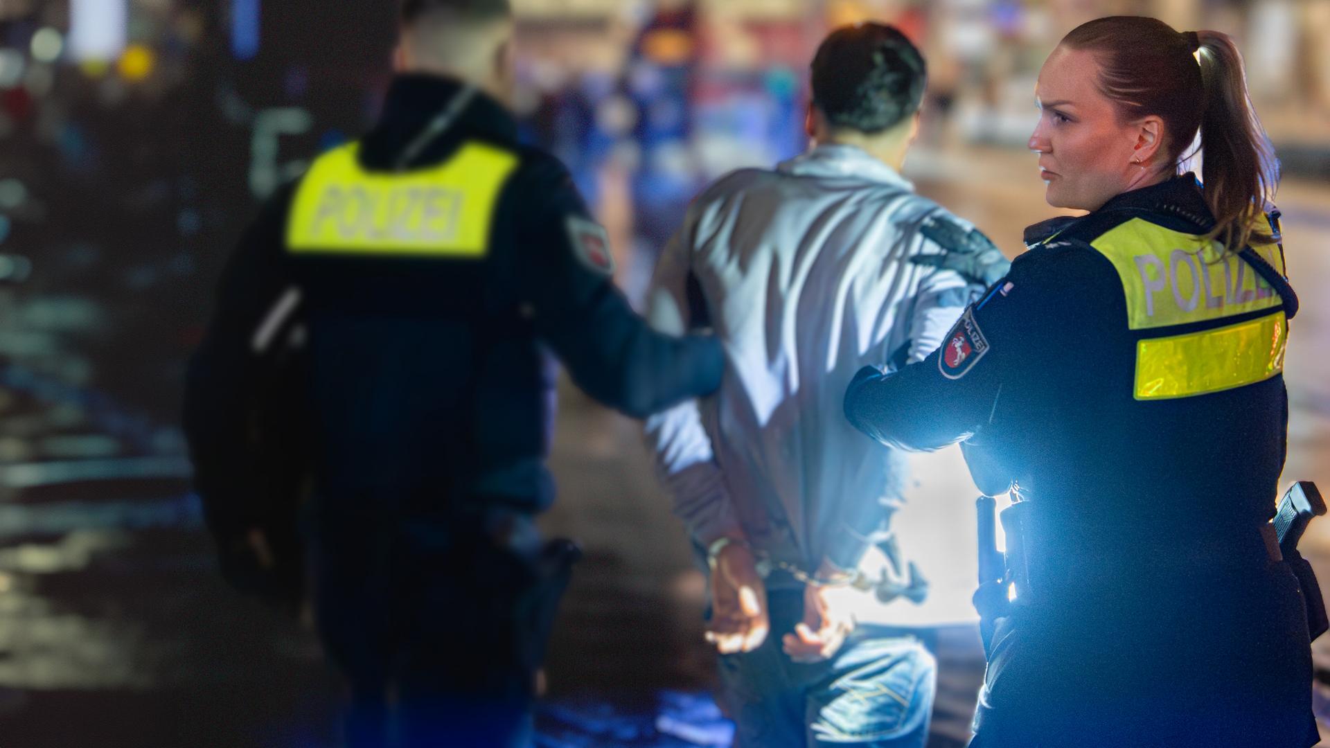 Ein Mann in Rückenansicht wird von einer Polizistin und einem Polizisten abgeführt.