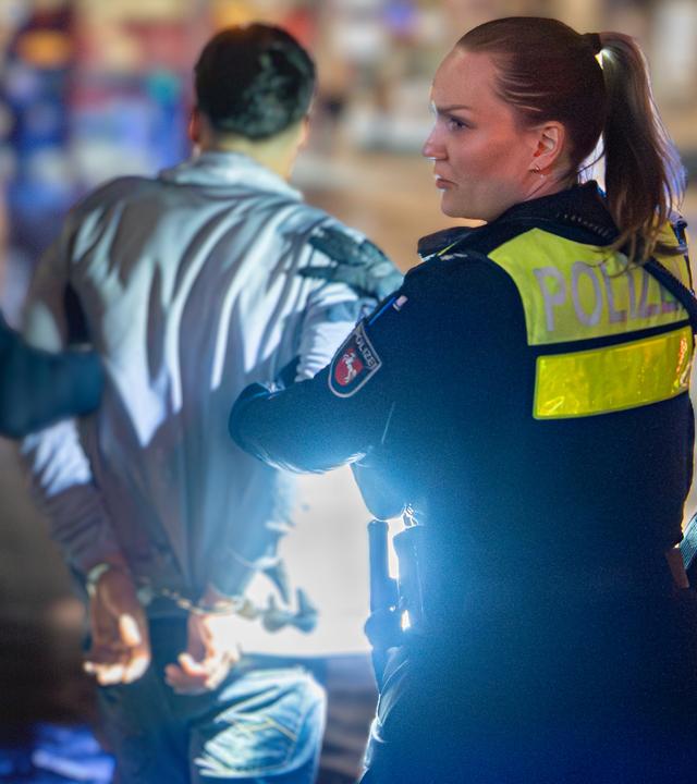 Ein Mann in Rückenansicht wird von einer Polizistin und einem Polizisten abgeführt.
